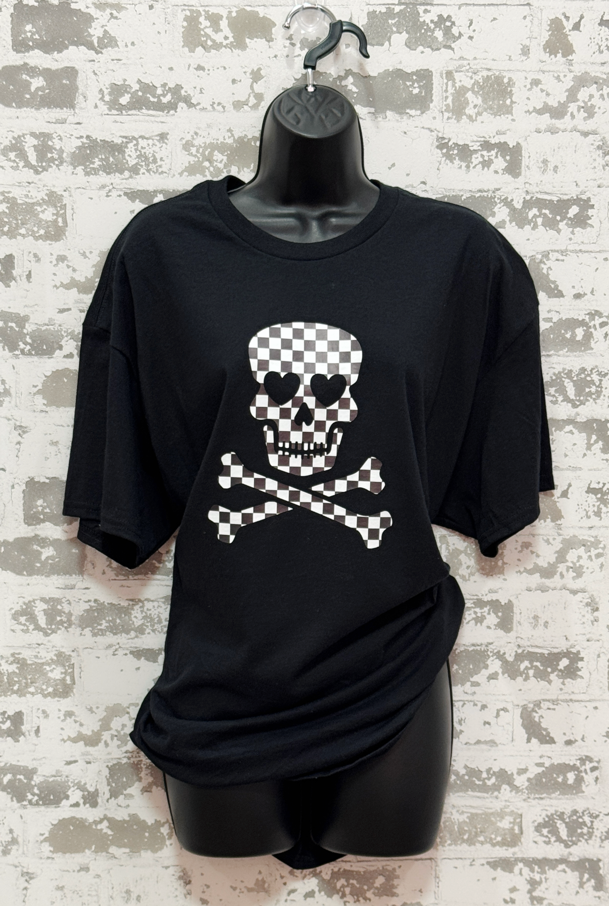 Black t-shirt with a skull and crossbones design on a mannequin against a textured wall.