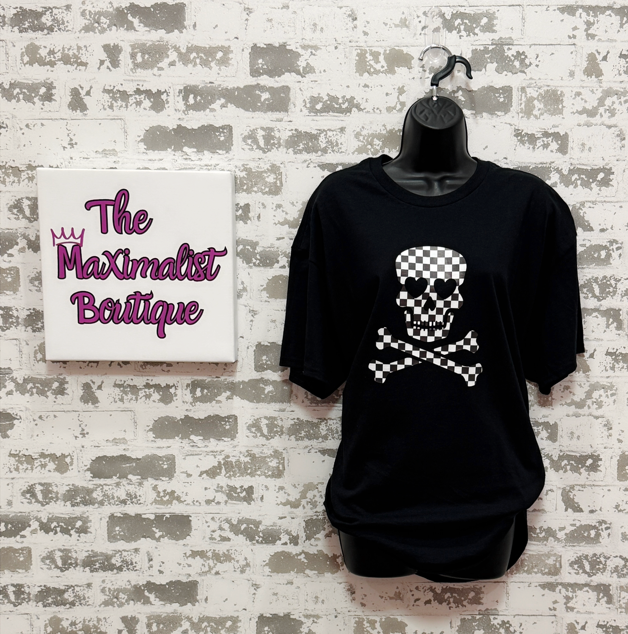 Black t-shirt with skull design on a mannequin against a textured wall with 'The Maximalist Boutique' sign.
