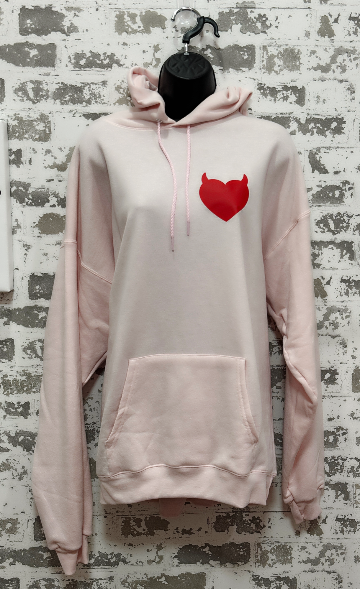 Pink hoodie with a red heart design on a textured wall background