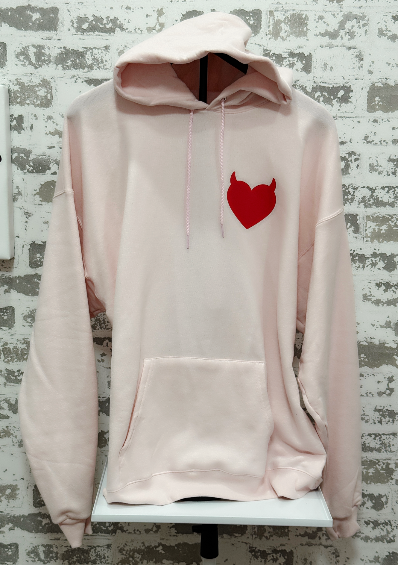 Pink hoodie with a red heart design on a textured wall background