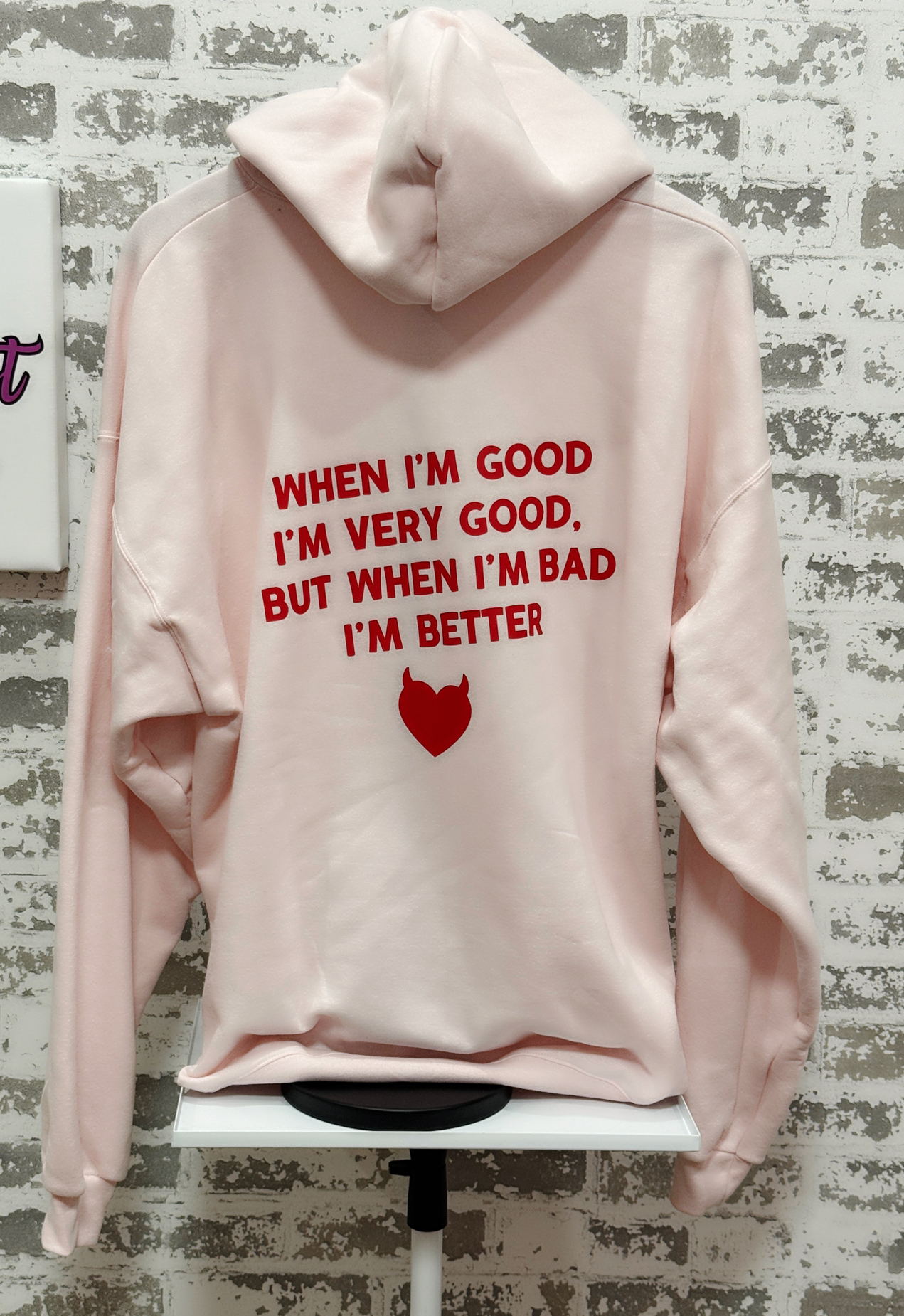 Pink hoodie with red text and a red heart graphic on a textured gray background