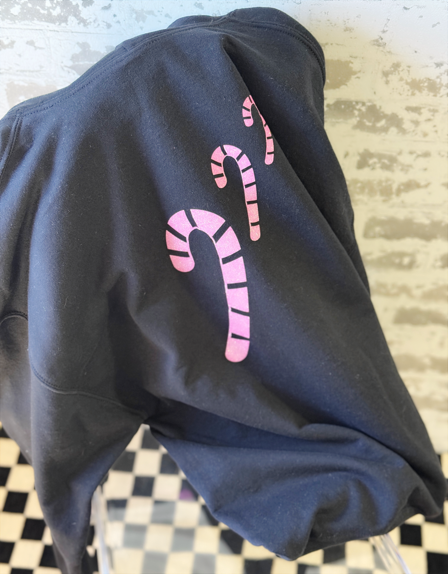 Black hoodie with pink candy cane design on a checkered floor background