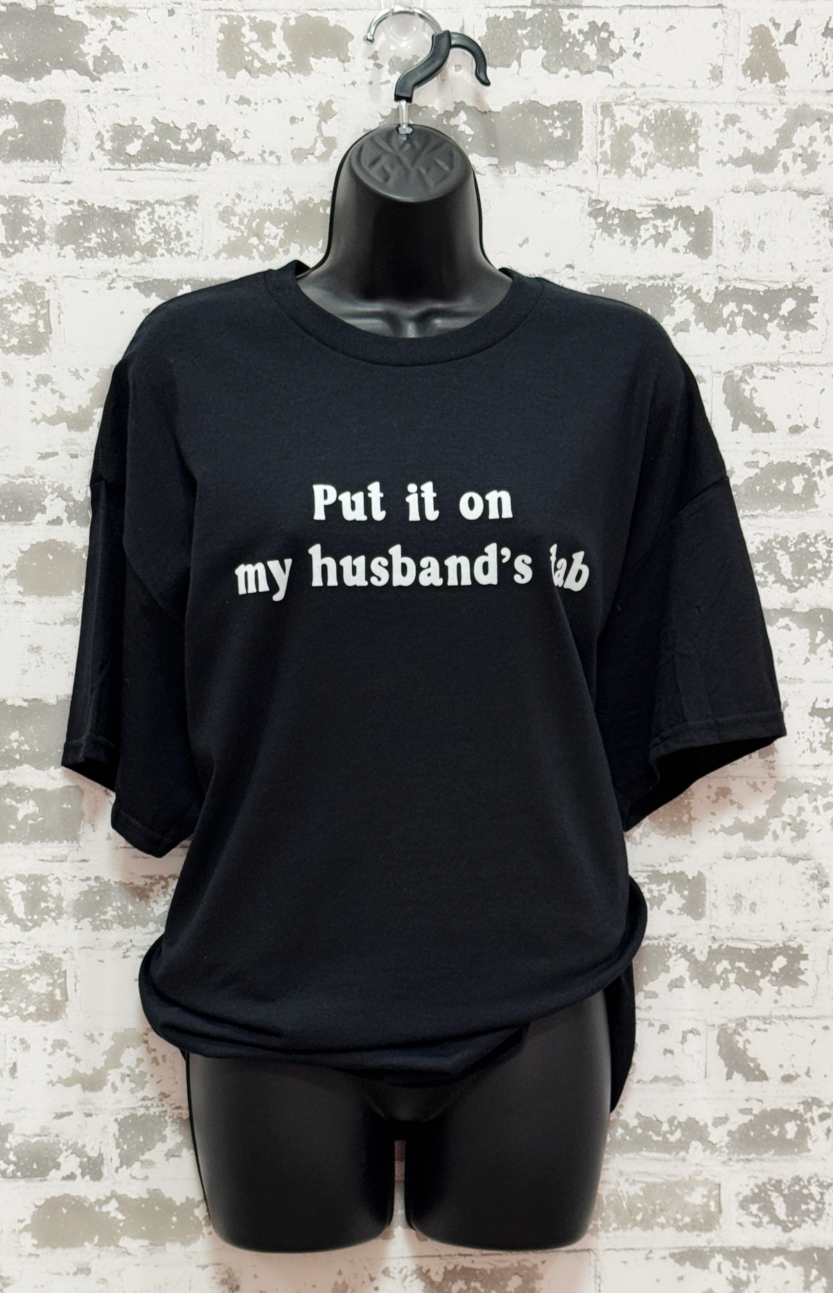 Black t-shirt with text on a mannequin against a textured wall background