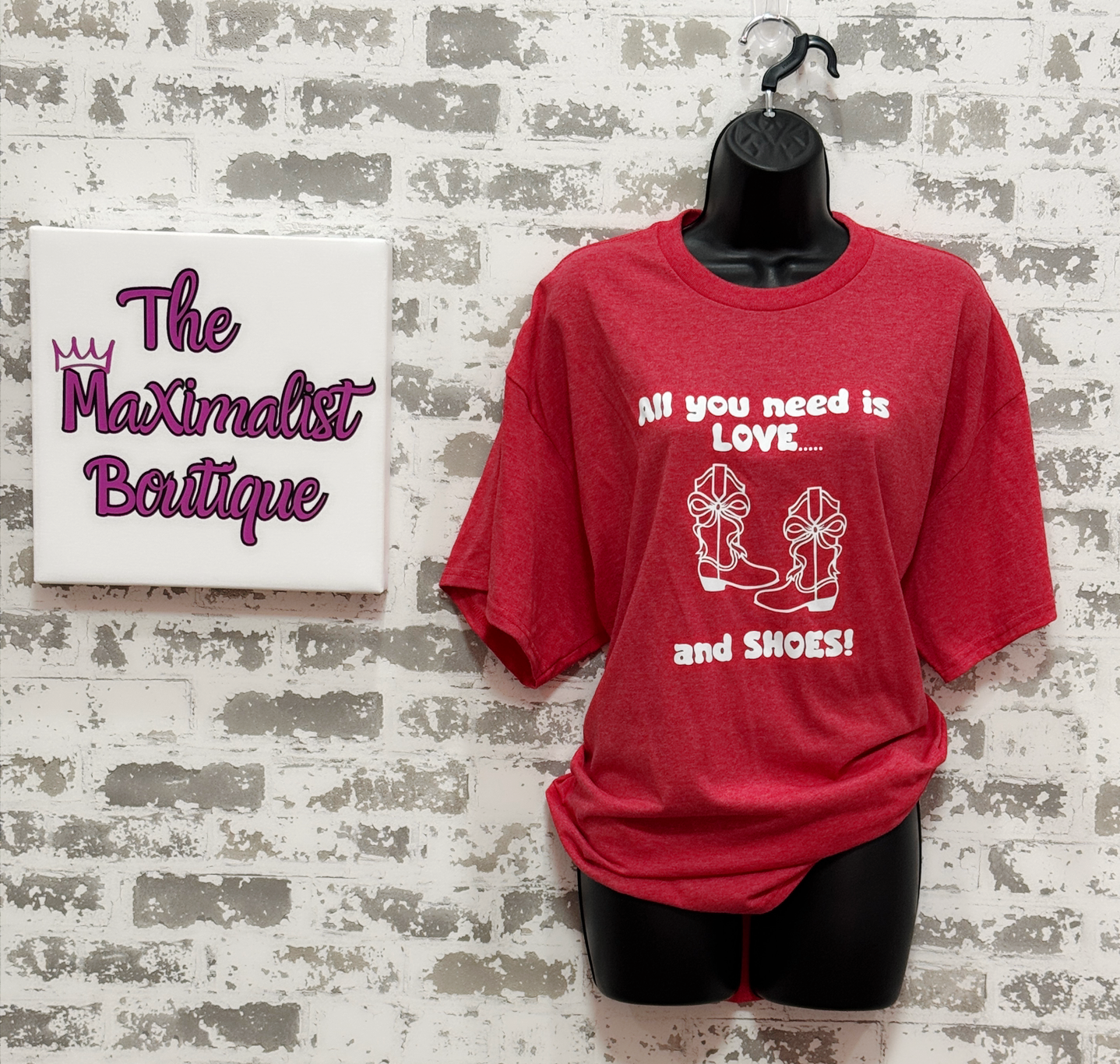 Red t-shirt with text on a mannequin against a textured wall with 'The Maximalist Boutique' sign.