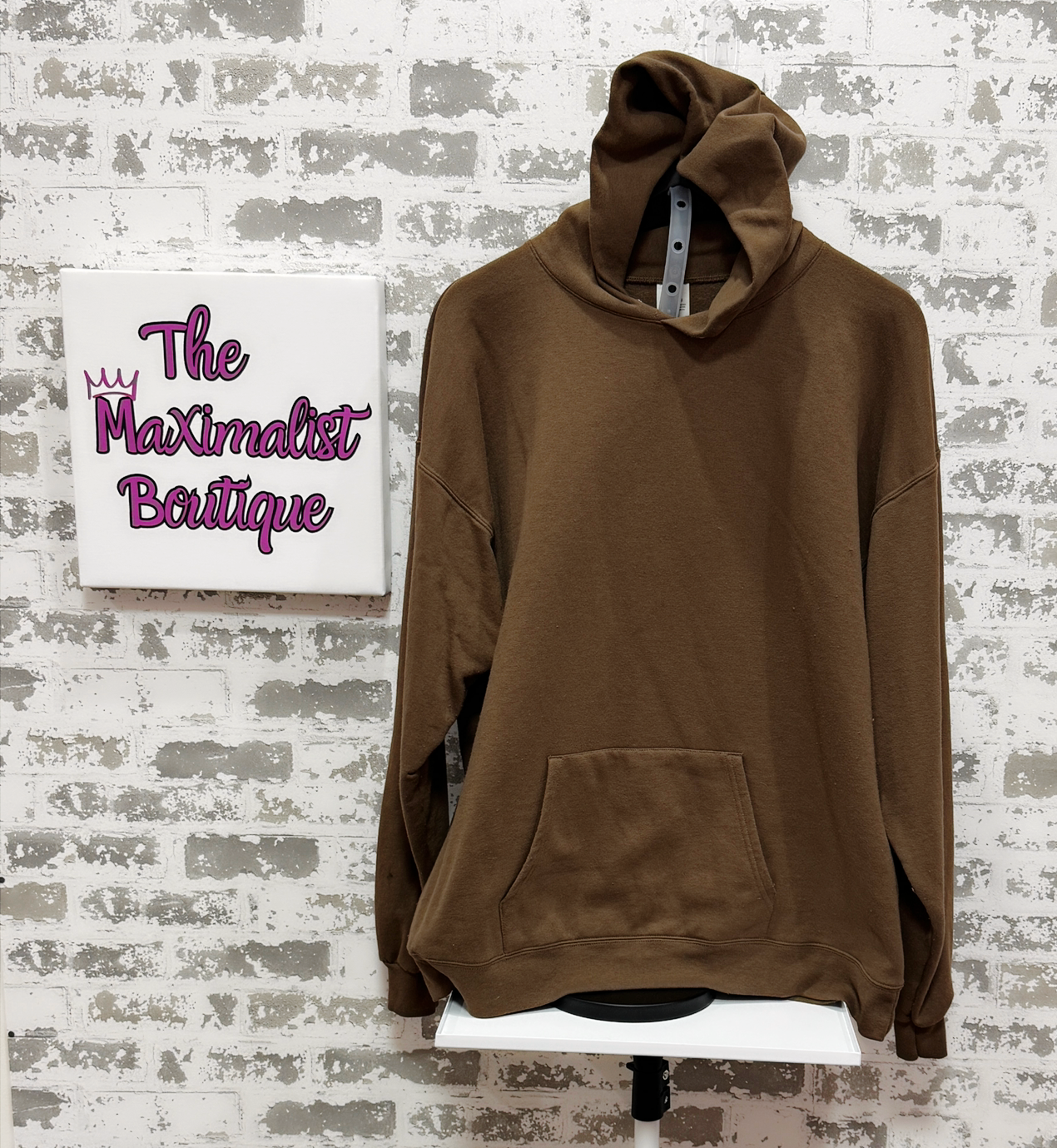 Brown hoodie on a stand with 'The Maximalist Boutique' sign in the background