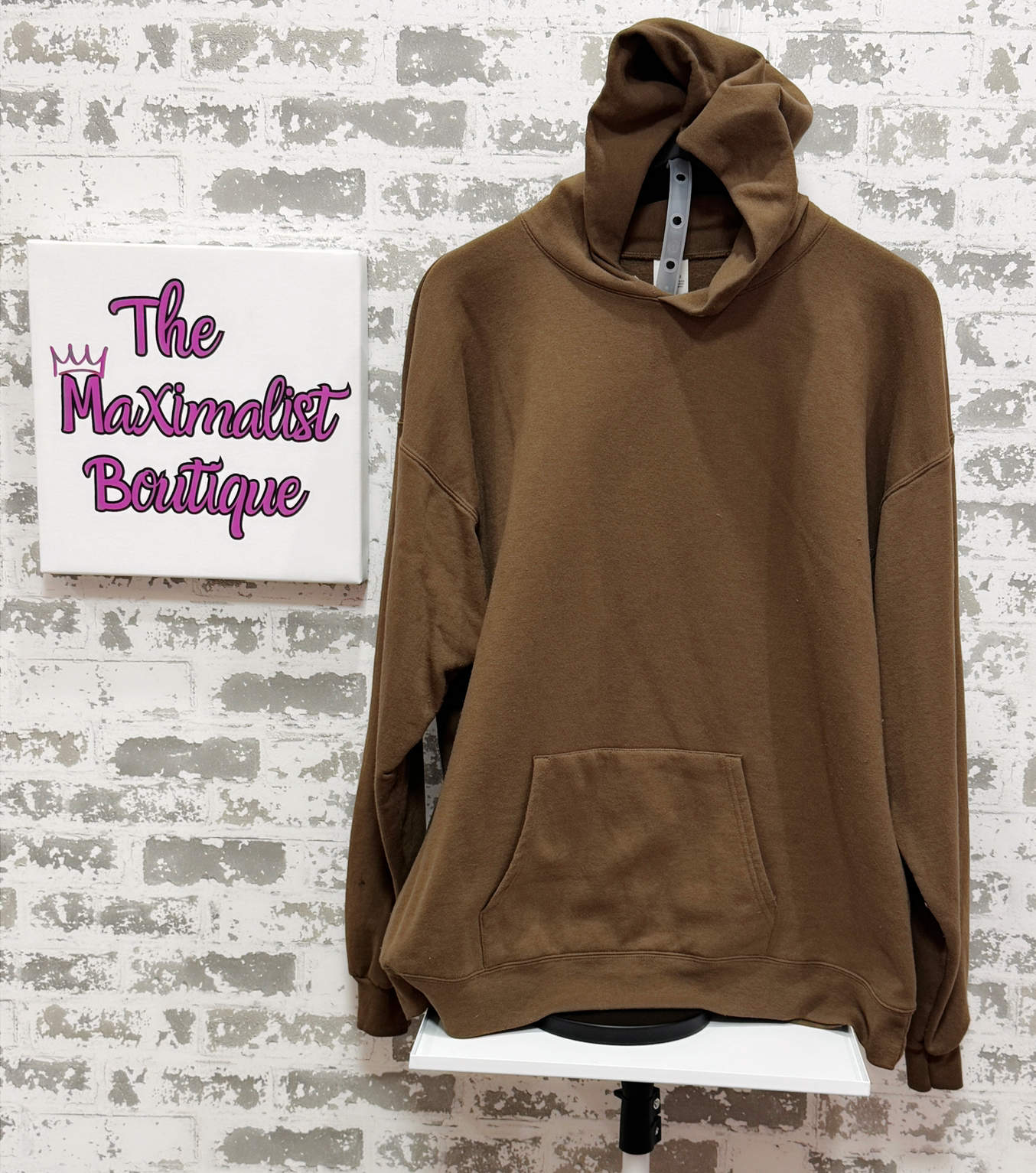 Brown hoodie on a stand with 'The Maximalist Boutique' sign in the background