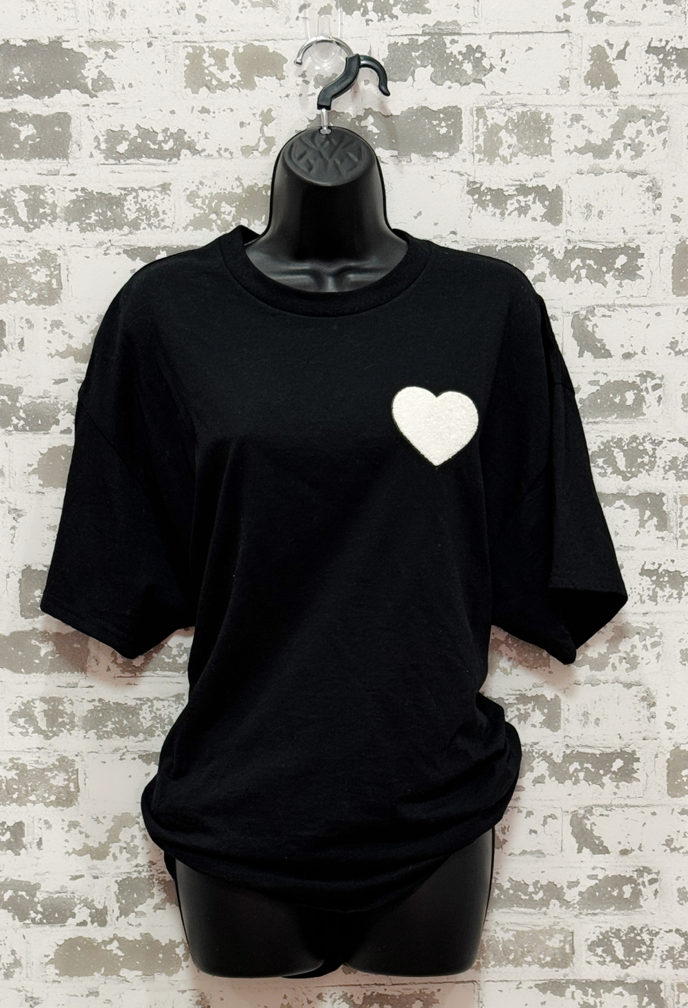 Black t-shirt with a white heart design on a mannequin against a textured wall background