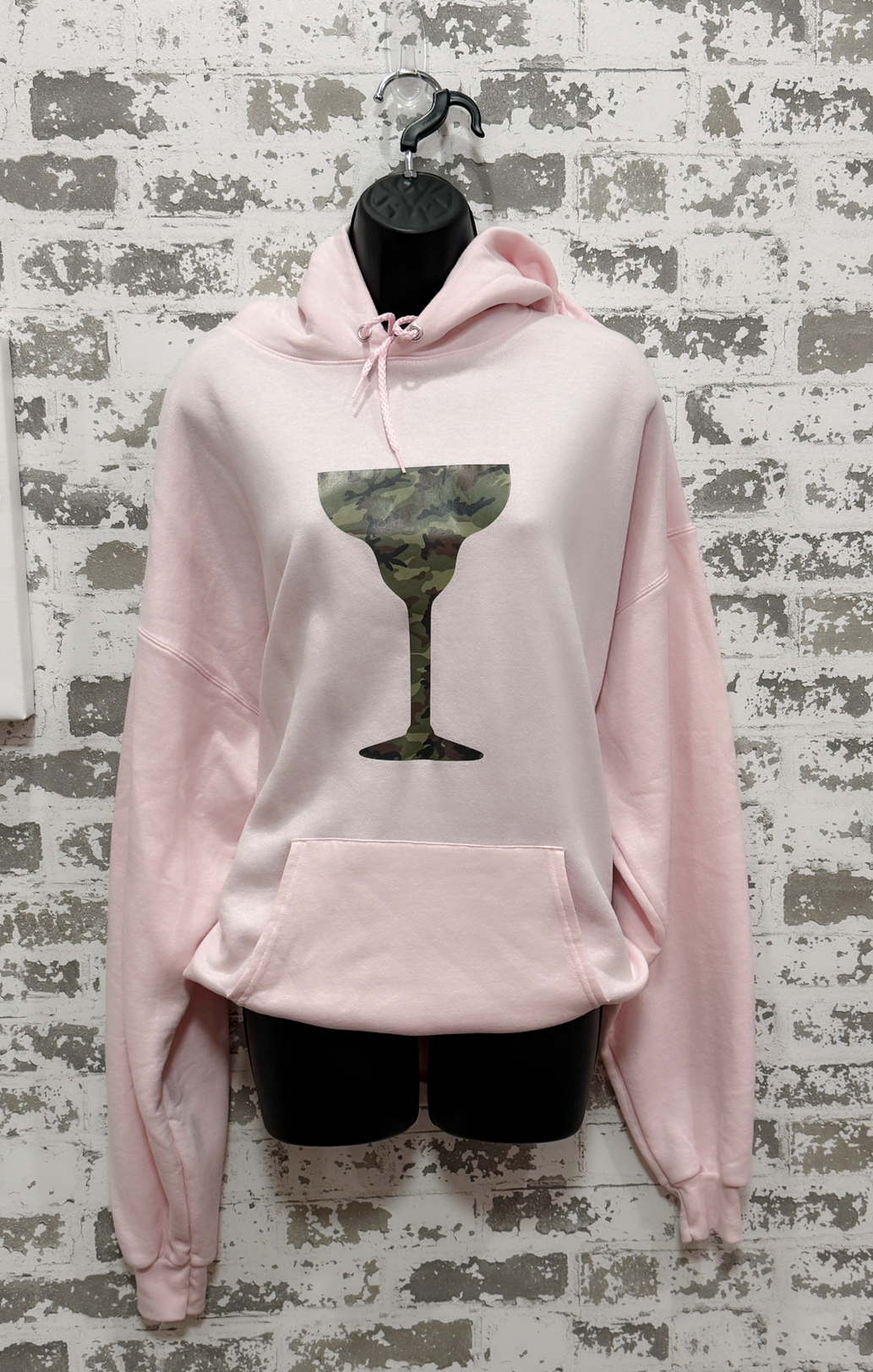 Pink hoodie with a green wine glass design on a textured wall background