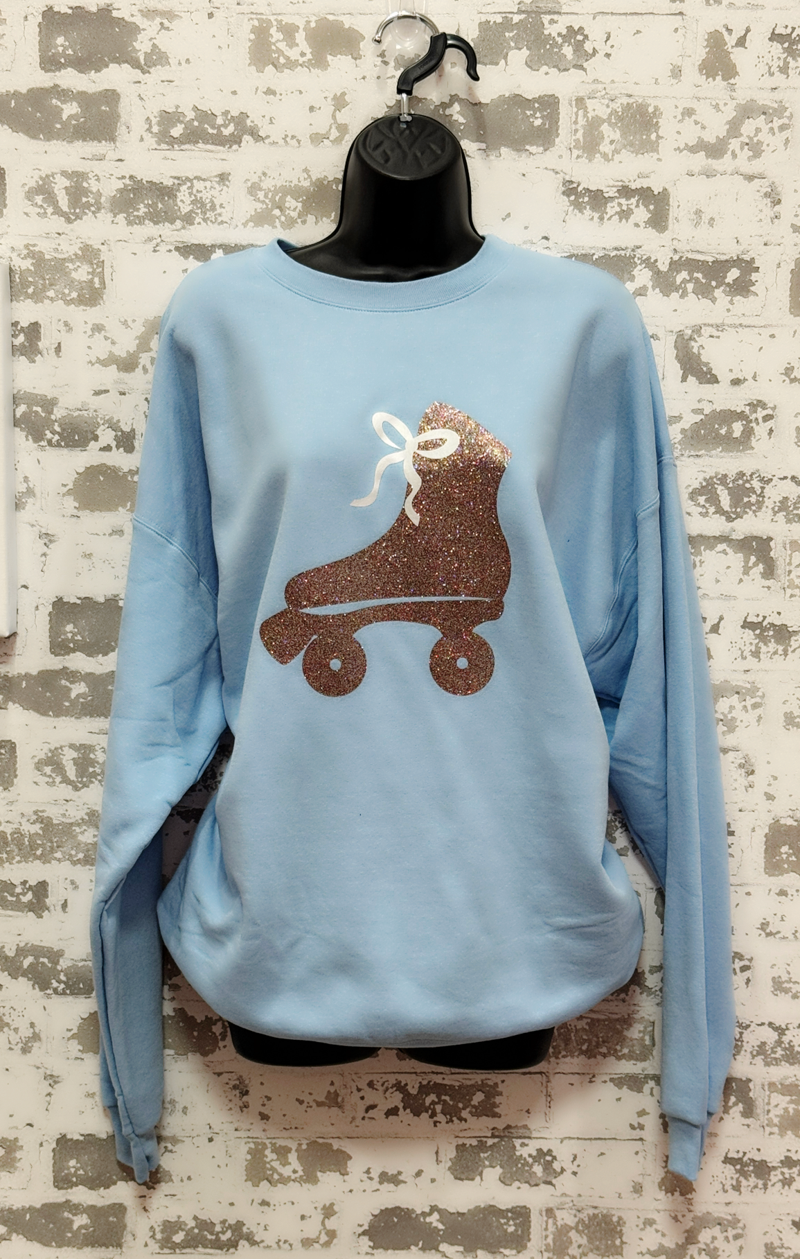 Light blue sweatshirt with a glitter roller skate graphic on a textured brick wall background