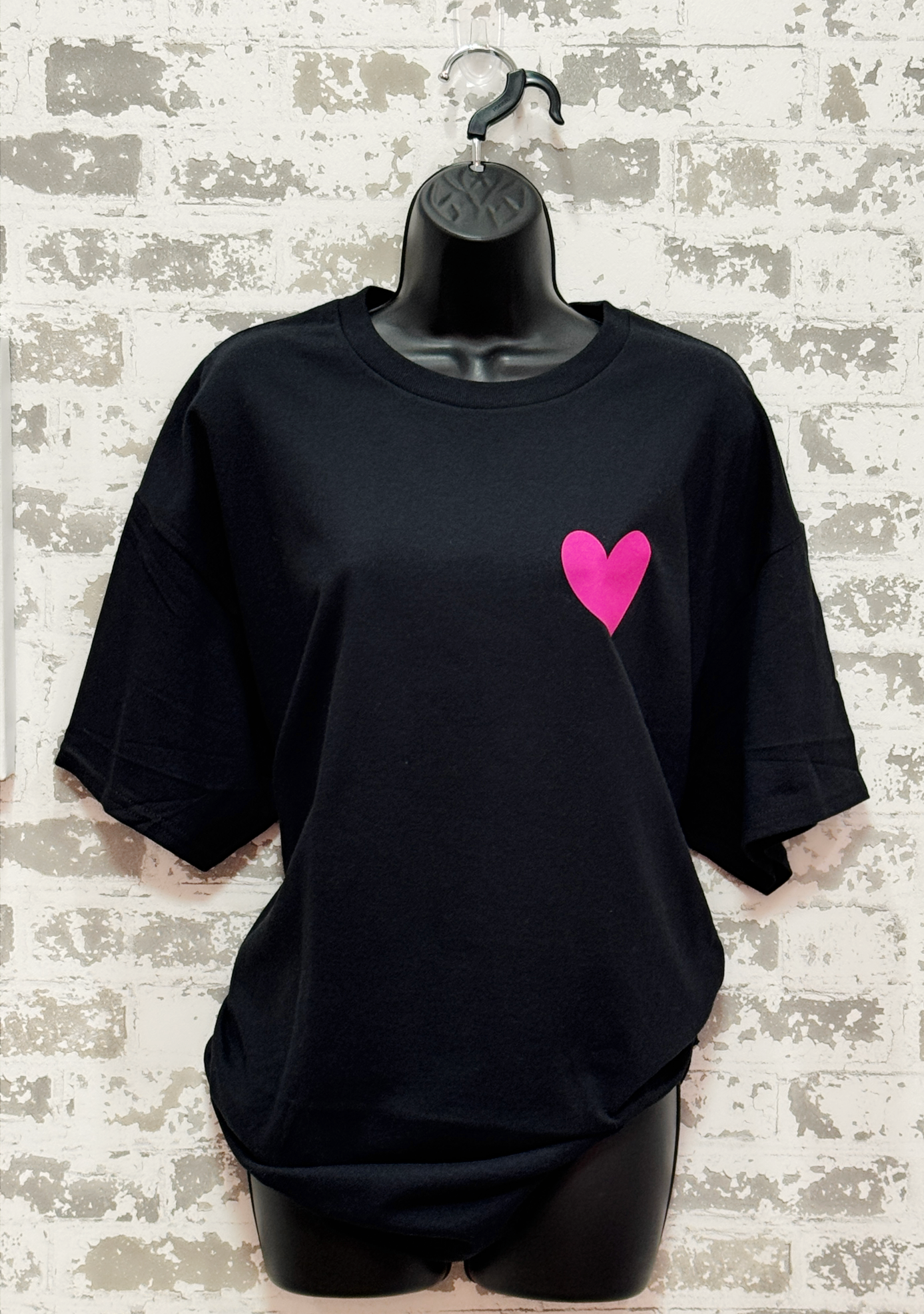 Black t-shirt with a pink heart on a mannequin against a textured wall background