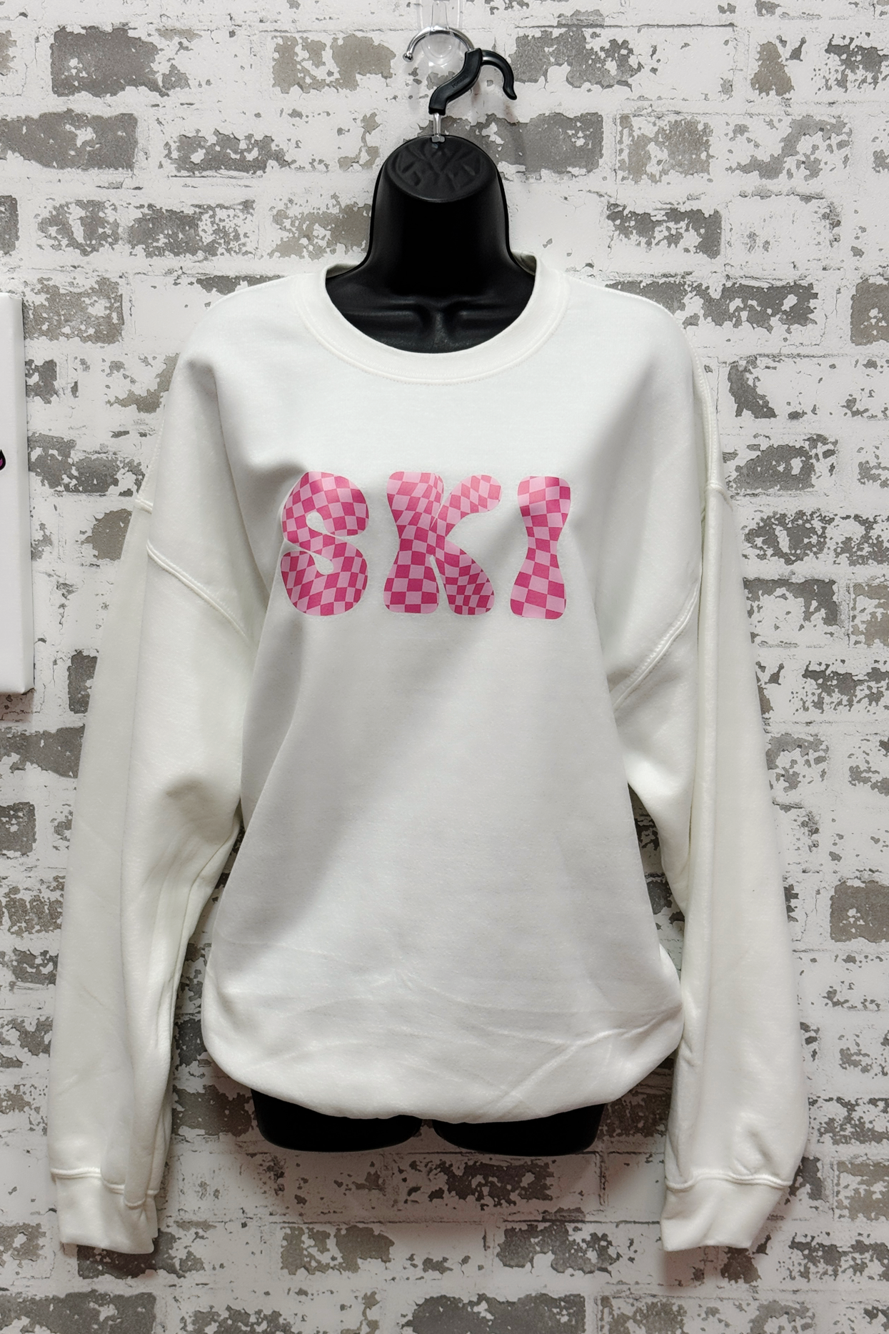 White sweatshirt with pink 'SKI' text on a textured wall background