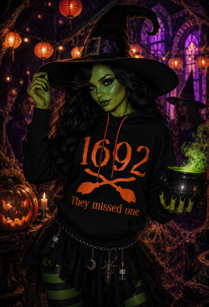 Witch wearing a black hoodie with orange "1692 they missed one" graphic and orange rhinestone strings