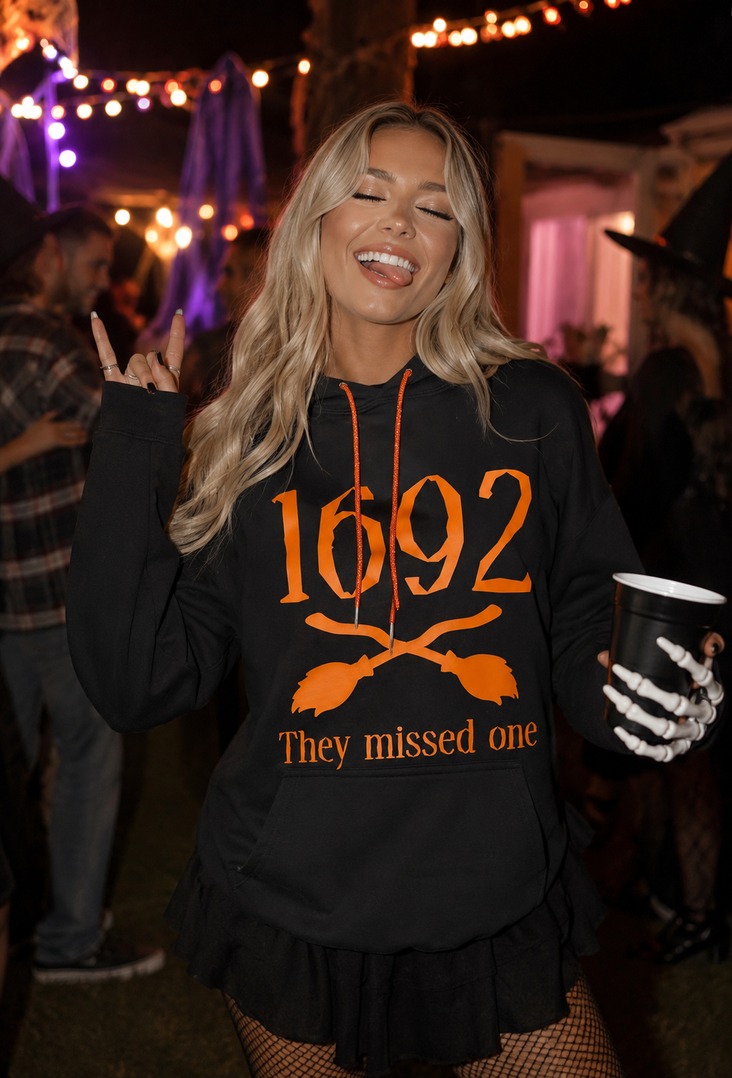 Model wearing a black hoodie with orange "1692 they missed one" graphic and orange rhinestone strings