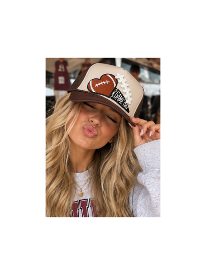 A cream and chocolate brown trucker hat featuring an embroidered football-heart patch with lace detailing and a GAME DAY pennant, captured in a high-quality product shot for The Maximalist Boutique.