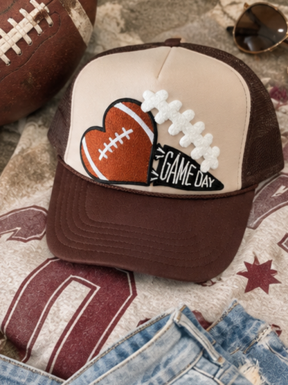 Cream and chocolate brown high-crown trucker hat featuring an embroidered football-heart patch and a GAME DAY pennant, displayed against a neutral background.