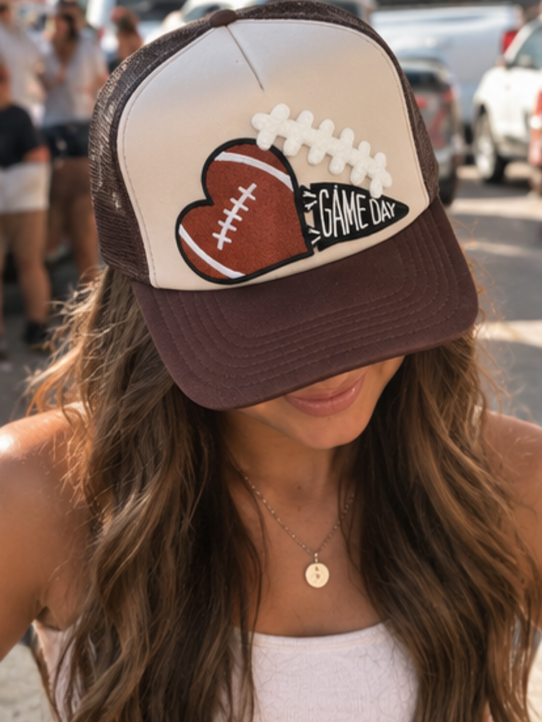 A cream and chocolate brown high-crown trucker hat featuring a football-heart patch and a GAME DAY pennant emblem, styled for a game-day outfit.
