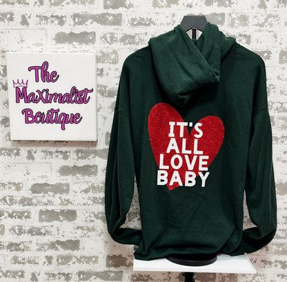 Green hoodie with red heart and white text on a mannequin against a textured wall with 'The Maximalist Boutique' sign.