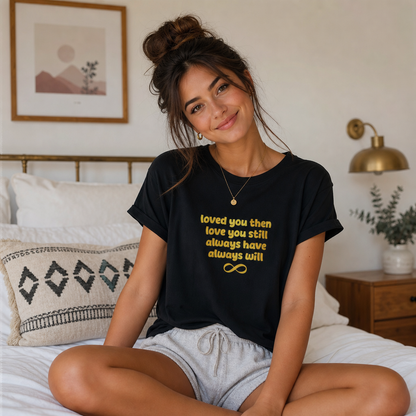 Woman wearing a black t-shirt with gold text in a bedroom setting