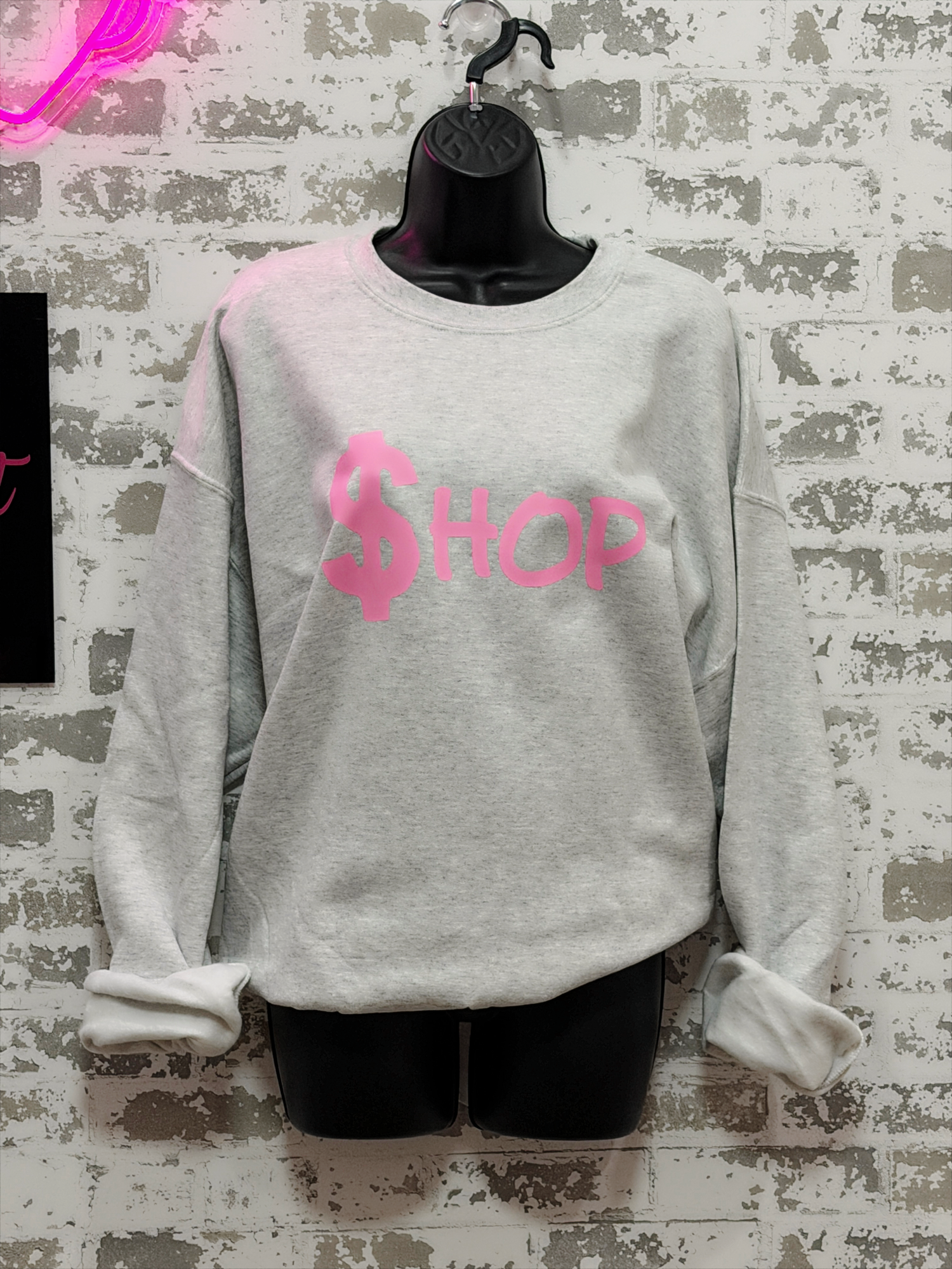Gray sweatshirt with pink text on a textured wall background