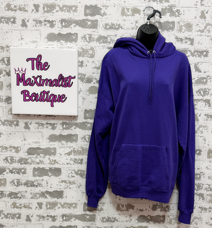 Purple hoodie on a mannequin against a textured wall with 'The Maximalist Boutique' sign.