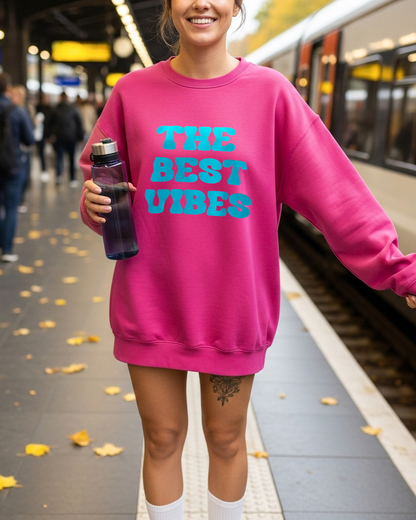 Person wearing a pink sweatshirt with 'THE BEST VIBES' text at a train station.