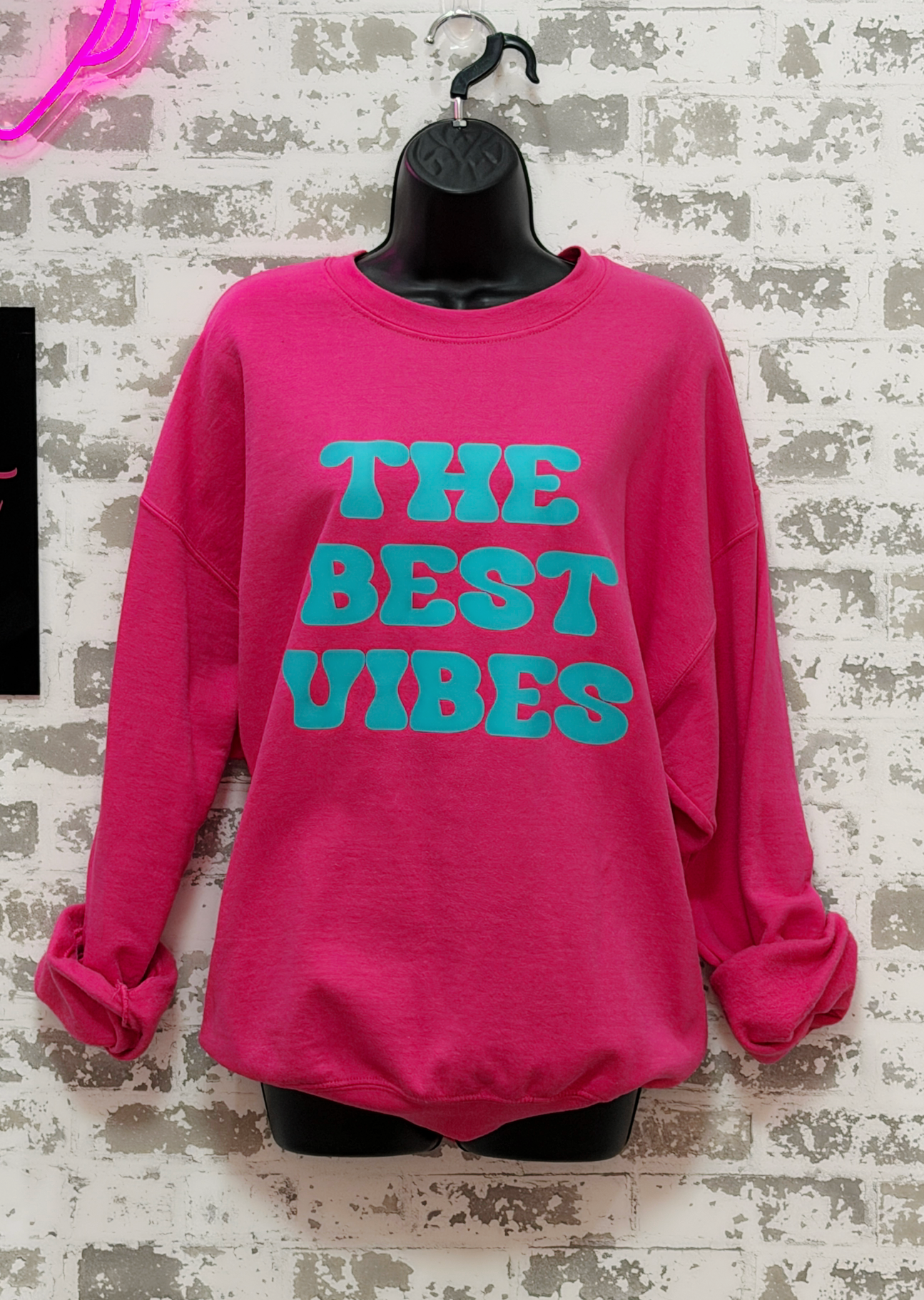 Pink sweatshirt with 'THE BEST VIBES' text on a textured white background