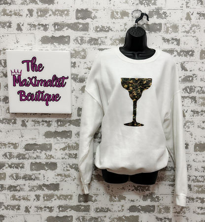 White sweatshirt with a camo design on a mannequin against a textured wall with 'The Maximalist Boutique' sign.