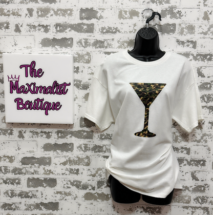 White t-shirt with camo print martini glass design on a mannequin against a brick wall with 'The Maximalist Boutique' sign.