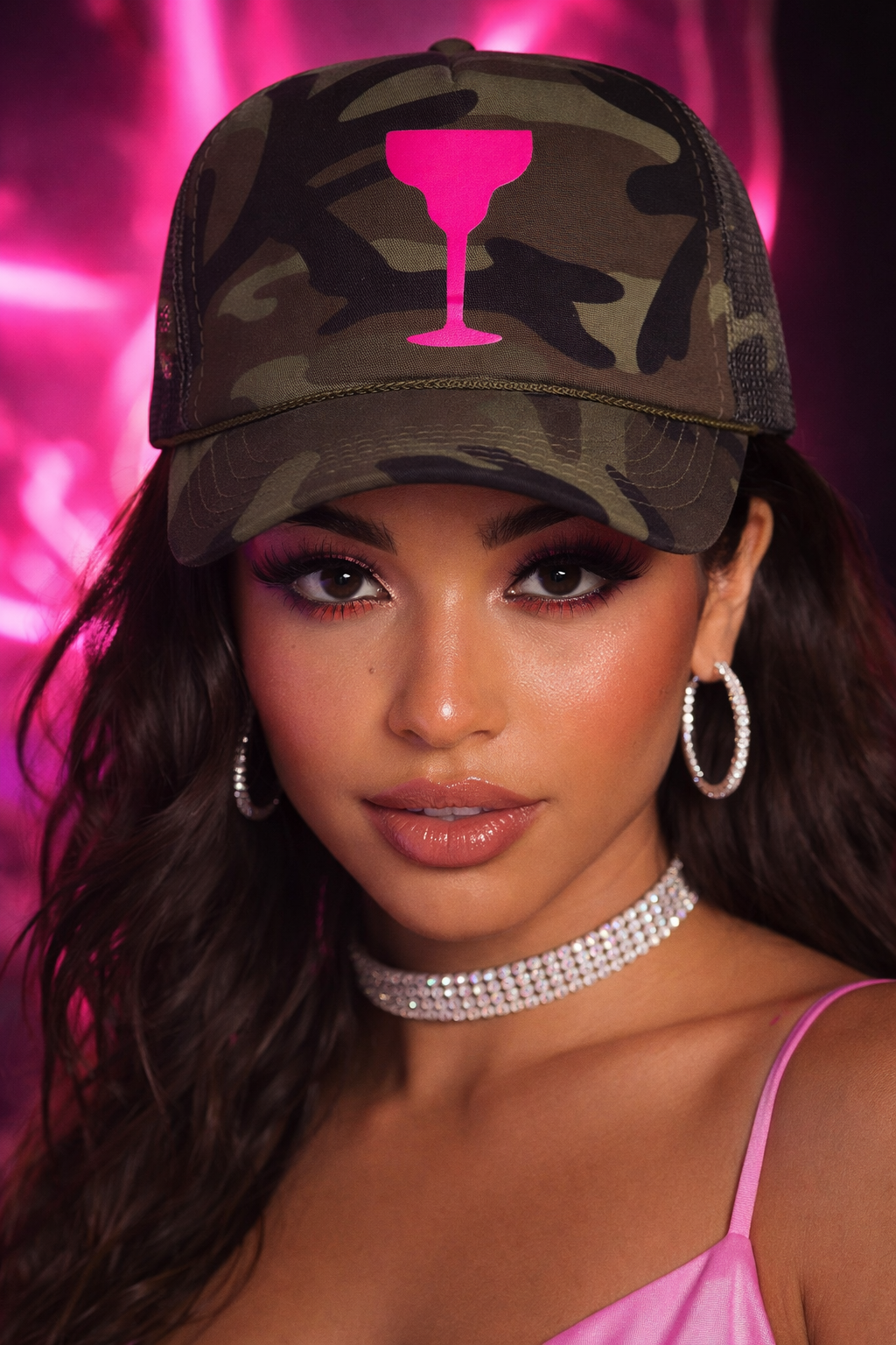 Woman wearing a camouflage cap with a pink drink icon against a pink background