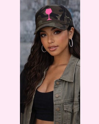 Woman wearing a camouflage cap with a pink wine glass design, gray jacket, and black top.