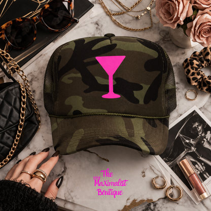 Camouflage cap with pink cocktail icon on a marble surface with jewelry and flowers.