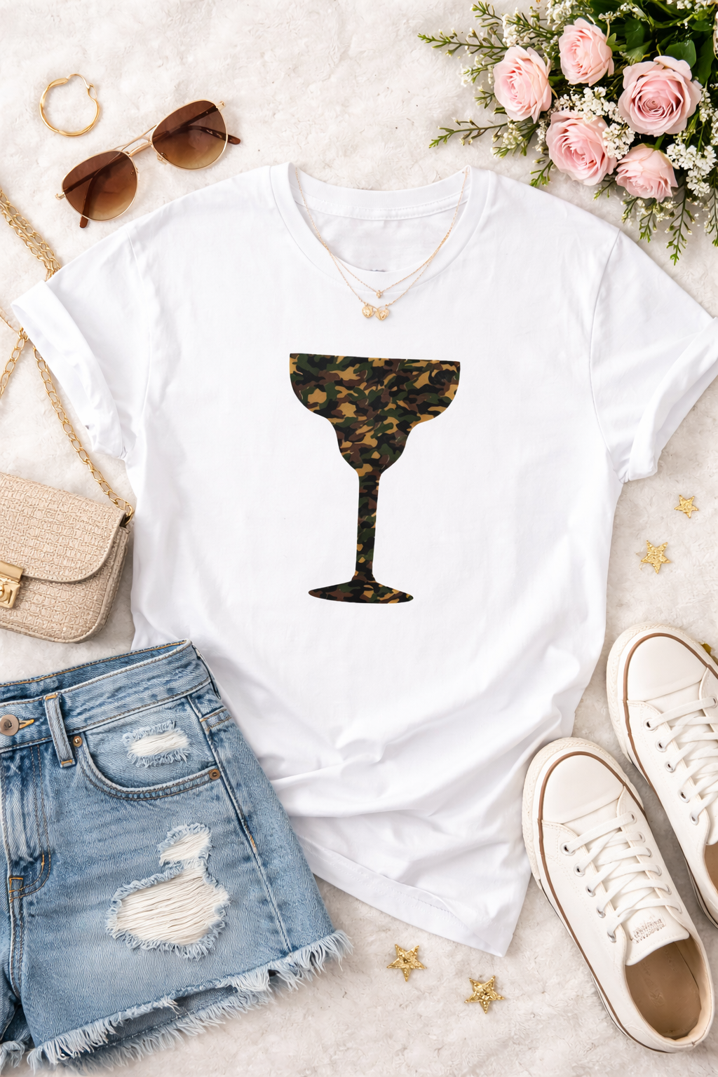 White t-shirt with camo print cocktail graphic, denim shorts, sneakers, sunglasses, handbag, and flowers on a light surface.