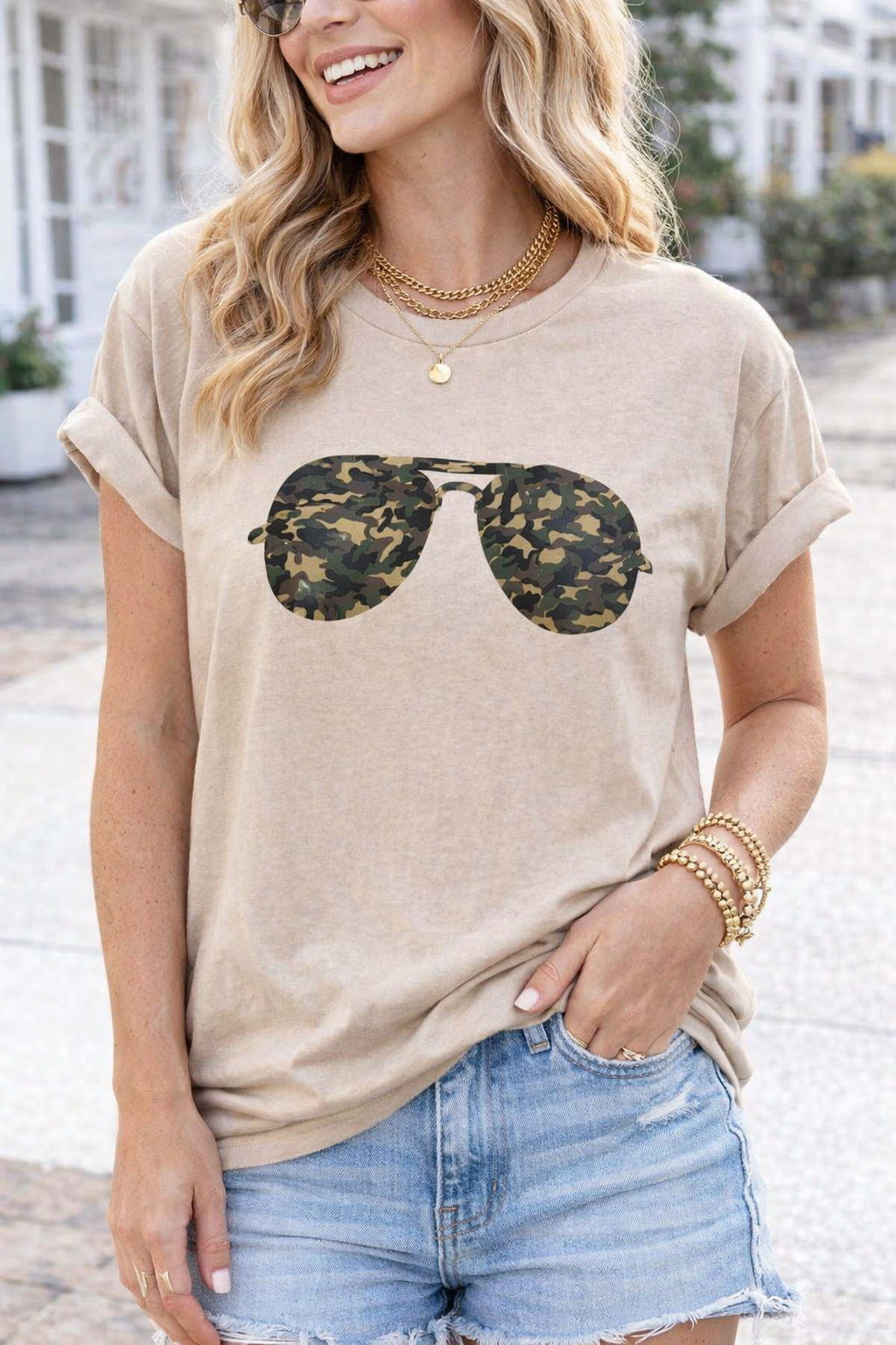 Woman wearing a beige t-shirt with sunglasses graphic and denim shorts outdoors.