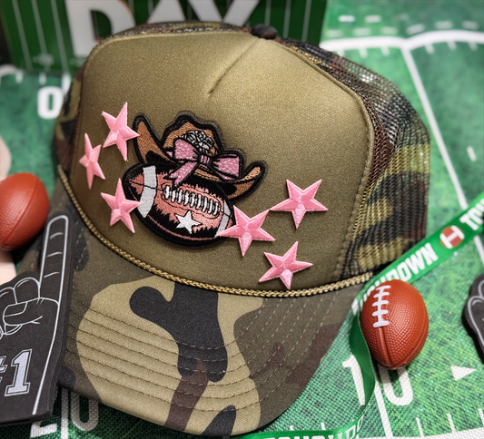 Camouflage baseball cap with pink star decorations and a football-themed patch on a sports-themed background.
