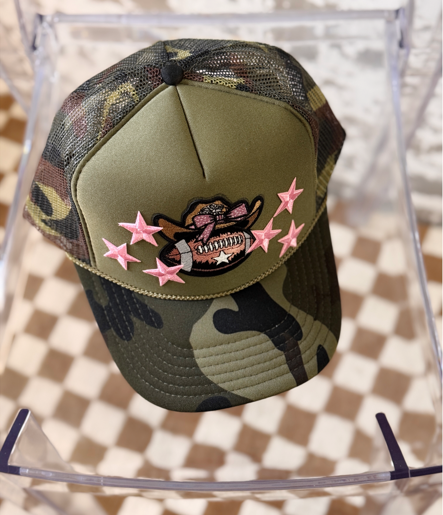 Camouflage baseball cap with pink stars and a design on a transparent stand.
