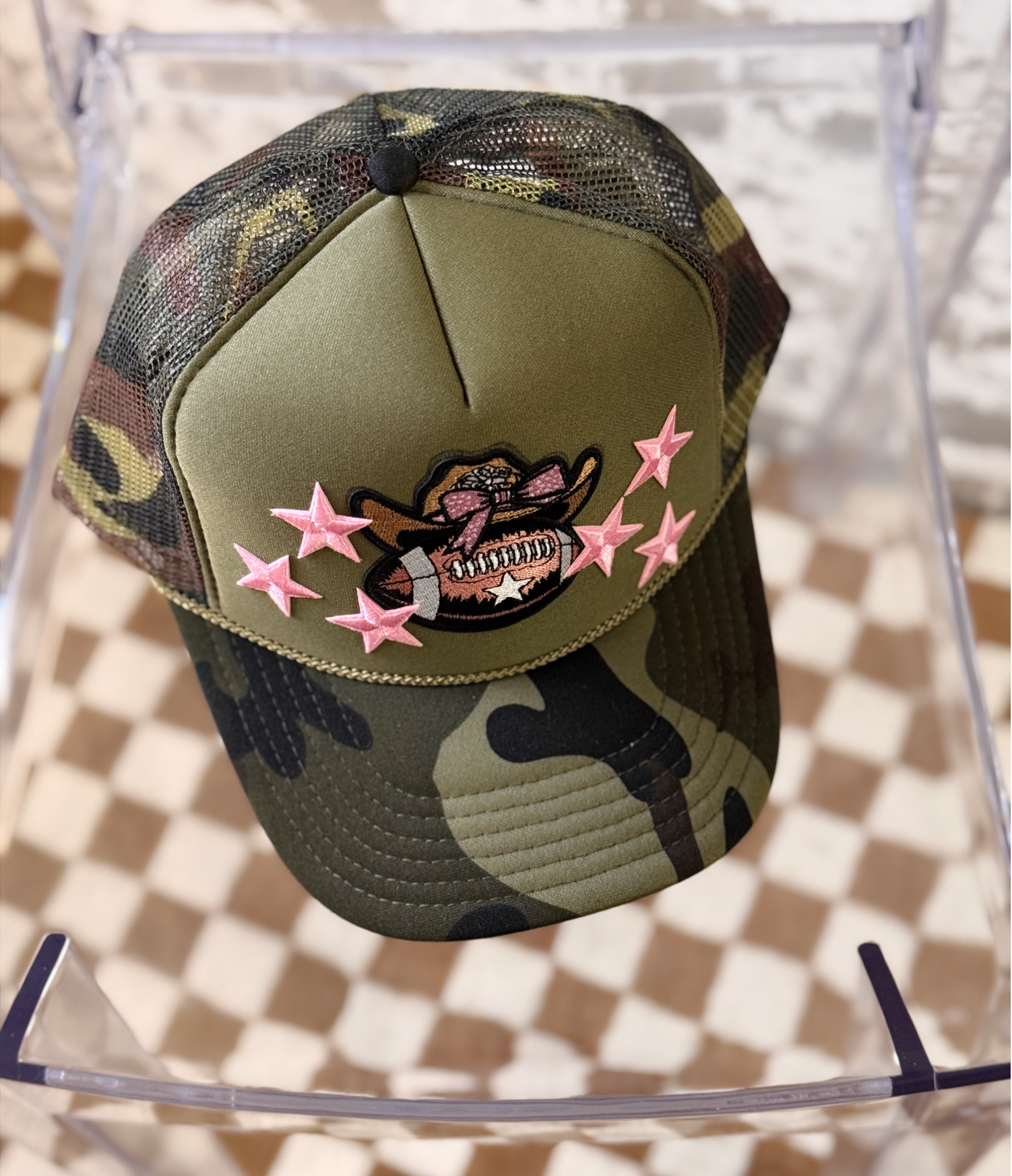 Camouflage baseball cap with pink stars and a design on a transparent stand.