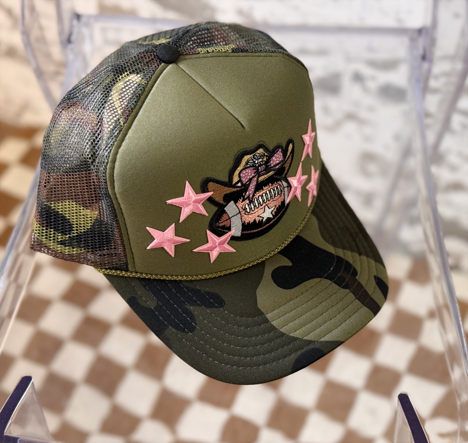 Camouflage baseball cap with pink star designs and a skull patch on a checkered background