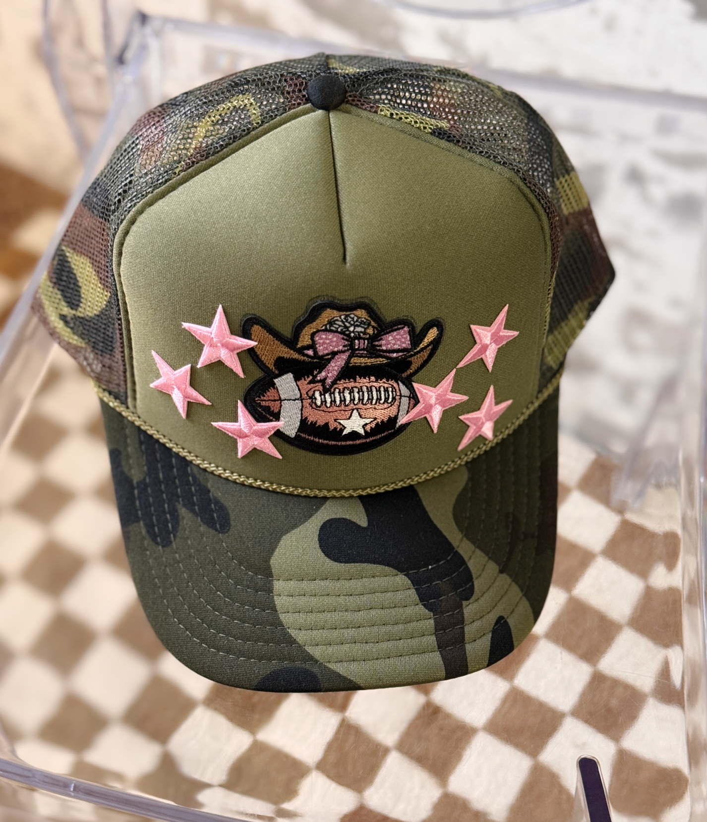 Camouflage baseball cap with pink stars and a patch on a checkered surface