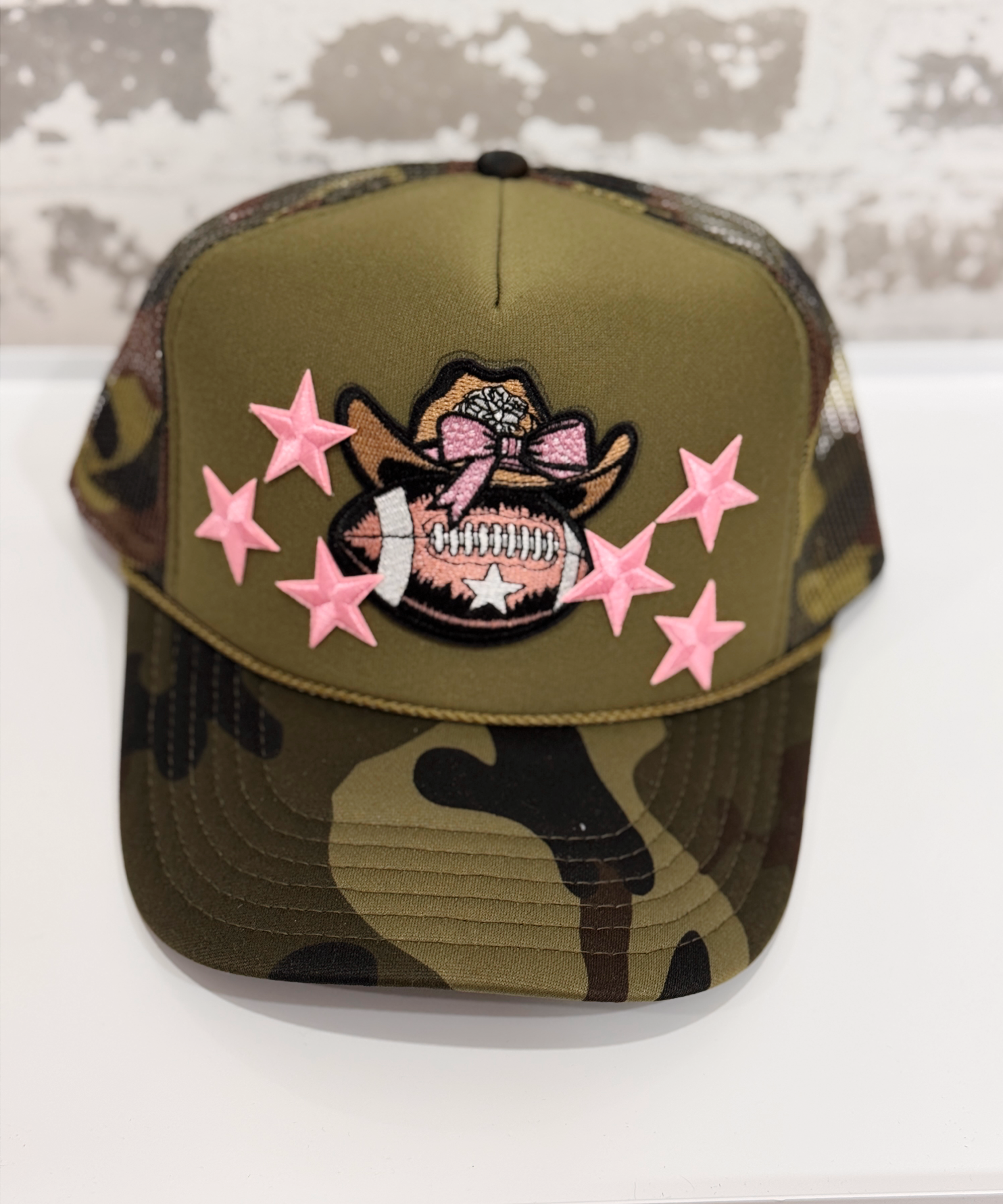 Camouflage cap with pink star decorations and a patch on a white surface.