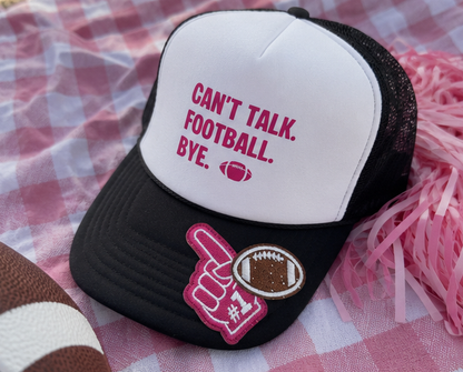 A black and white trucker hat with pink text reading 'CAN'T TALK. FOOTBALL. BYE.