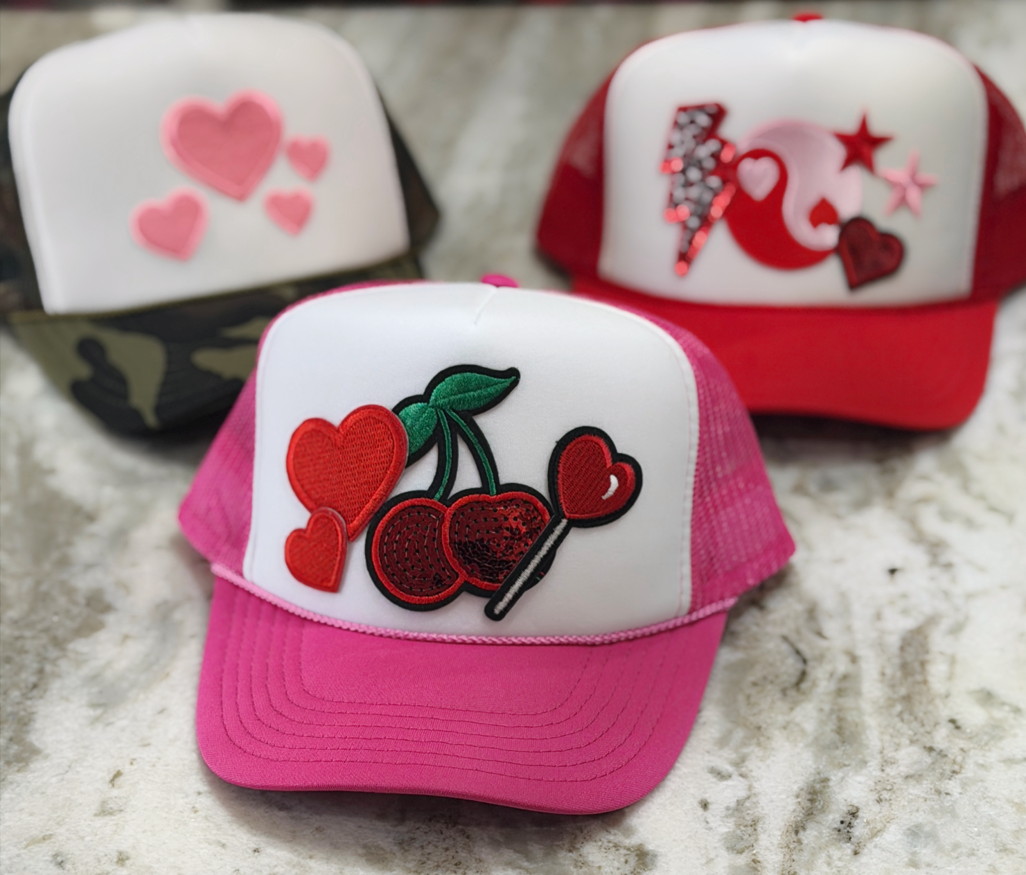 Three decorative caps with heart and cherry designs on a textured surface