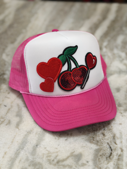 Pink and white cap with cherry and heart design on a textured surface