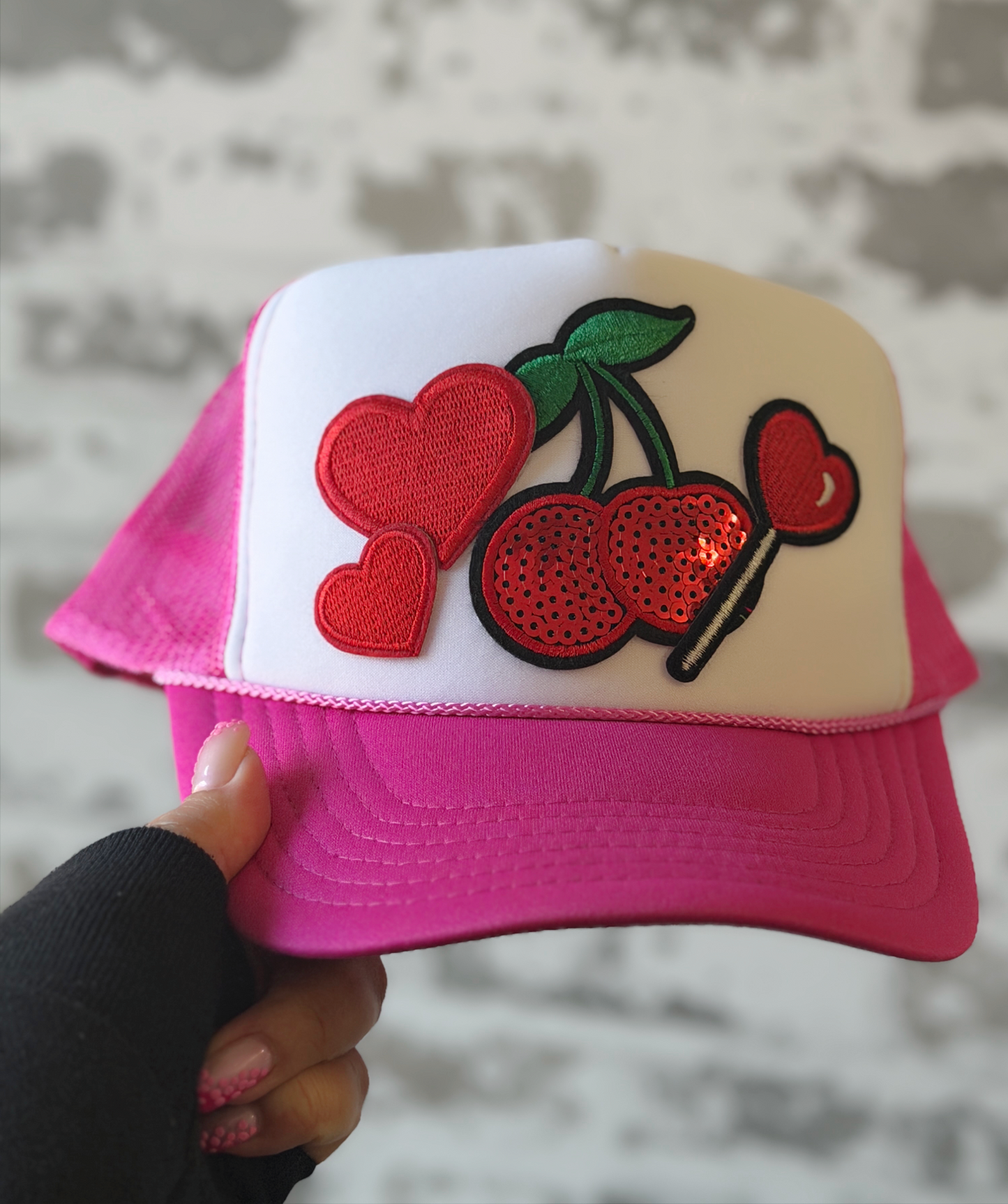 Pink and white cap with cherry design held against a neutral background