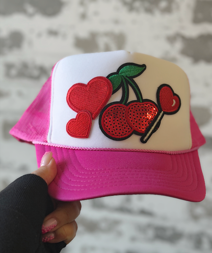 Pink and white cap with cherry design held against a neutral background