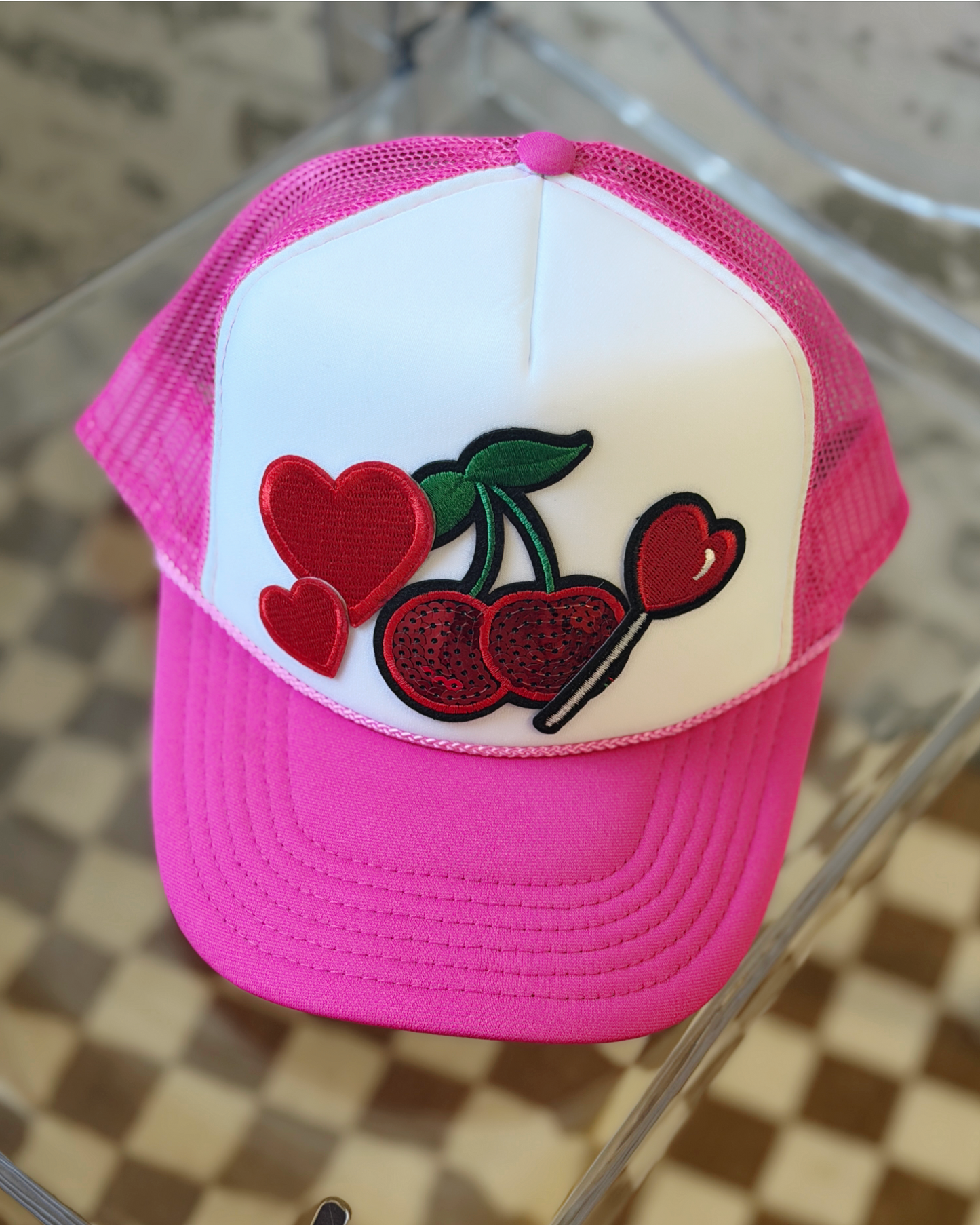 Pink and white cap with cherry and heart design on a glass surface