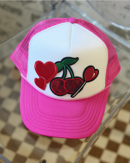 Pink and white cap with cherry and heart design on a glass surface
