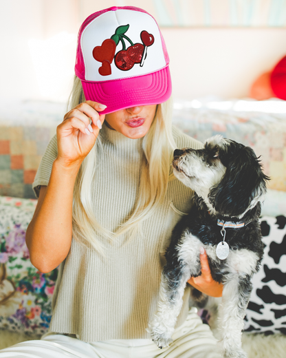 Person wearing a pink cap with cherry design holding a small black and white dog.
