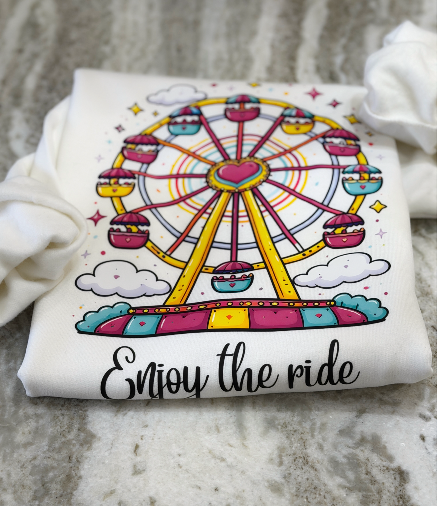 White t-shirt with a colorful Ferris wheel design and 'Enjoy the ride' text on a textured surface.