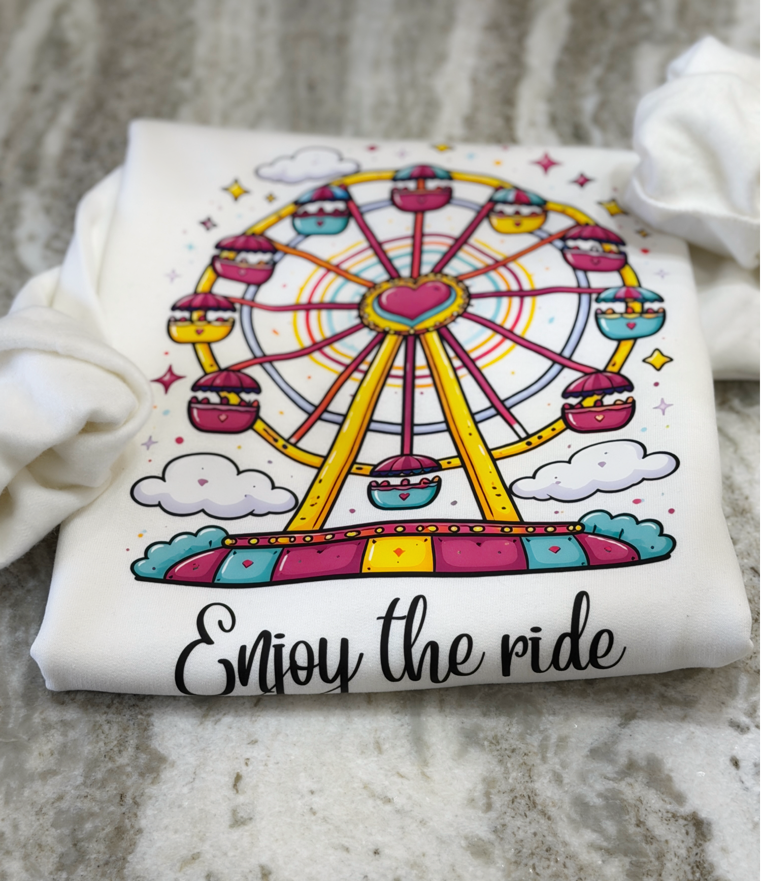 White t-shirt with a colorful Ferris wheel design and 'Enjoy the ride' text on a textured surface.