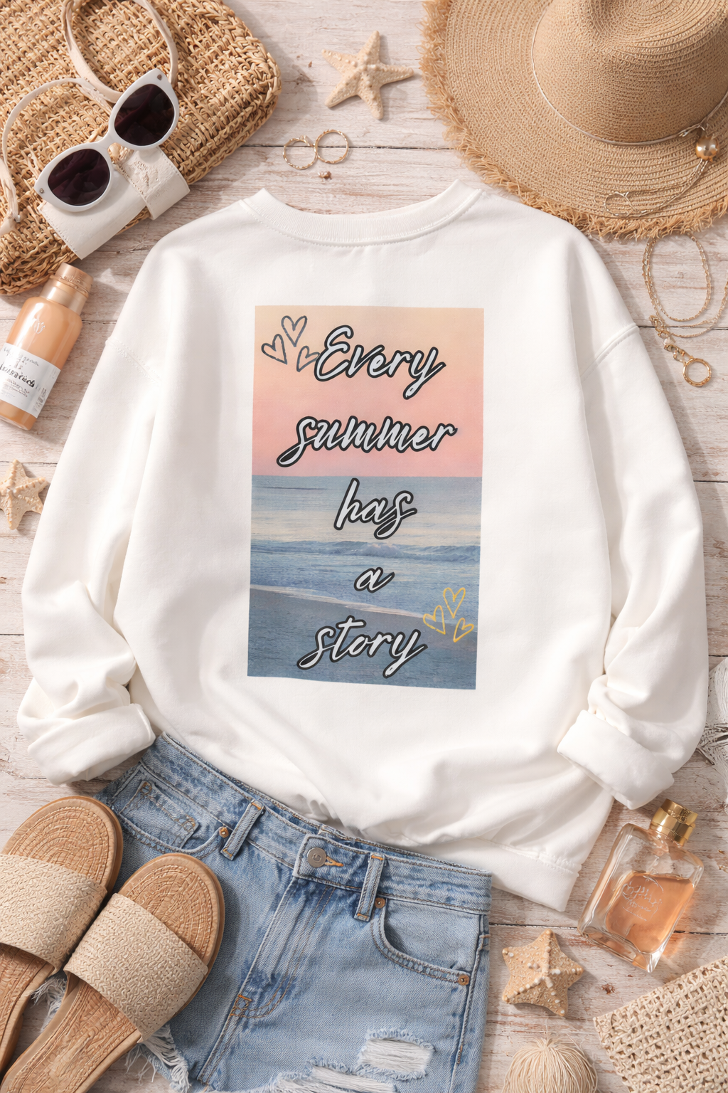 White sweatshirt with a beach-themed design and text, surrounded by summer accessories on a wooden surface.